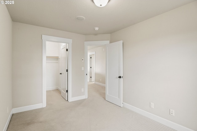 unfurnished bedroom featuring a closet, light colored carpet, baseboards, and a spacious closet