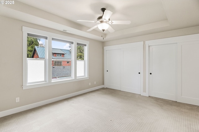 unfurnished bedroom with baseboards, light colored carpet, a tray ceiling, and multiple closets