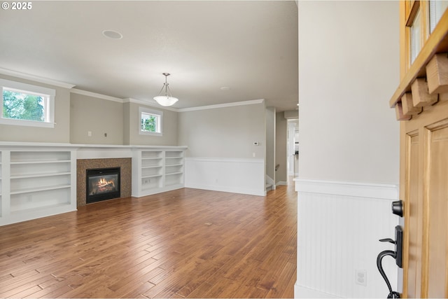 unfurnished living room with ornamental molding, a wealth of natural light, a glass covered fireplace, and wood finished floors