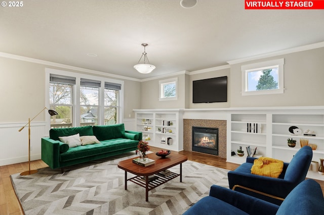 living area featuring ornamental molding, wainscoting, wood finished floors, and a healthy amount of sunlight