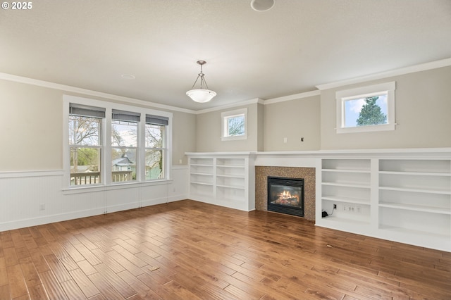 unfurnished living room featuring wood finished floors, ornamental molding, plenty of natural light, and a tile fireplace