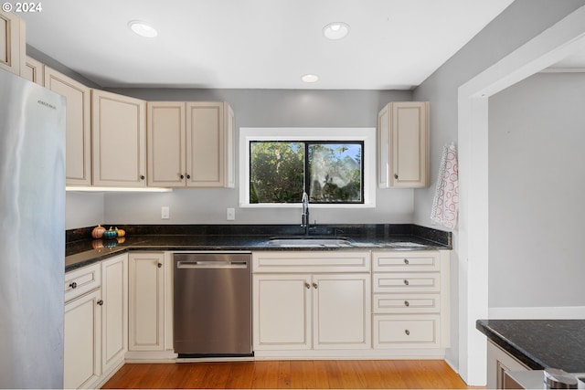 kitchen featuring dark stone countertops, cream cabinets, light wood-type flooring, stainless steel appliances, and sink