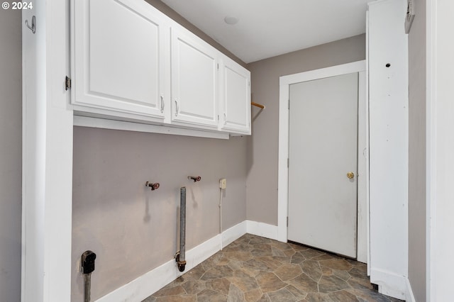 laundry room featuring stone finish flooring, cabinet space, and baseboards