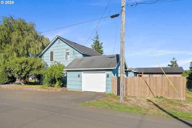 view of front of property featuring driveway, a shingled roof, a garage, and fence