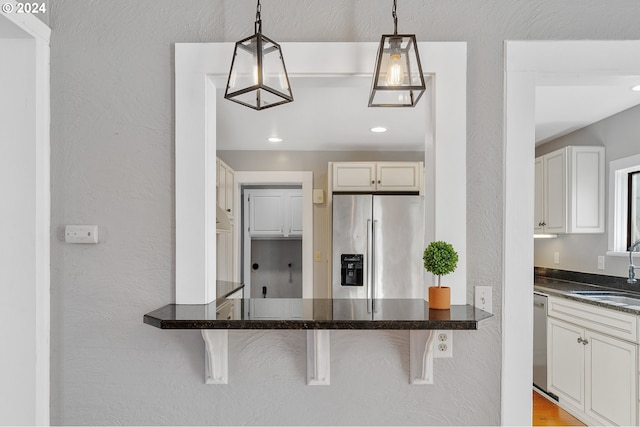 kitchen with pendant lighting, a textured wall, appliances with stainless steel finishes, a sink, and a kitchen bar