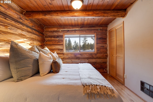 bedroom featuring wood ceiling, hardwood / wood-style floors, a closet, rustic walls, and beam ceiling