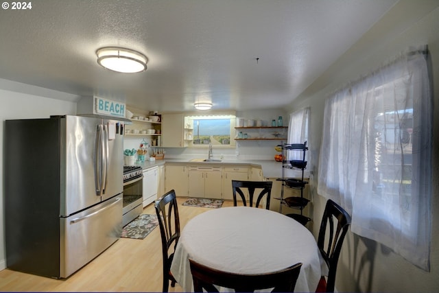 kitchen featuring light countertops, open shelves, stainless steel appliances, a sink, and light wood finished floors