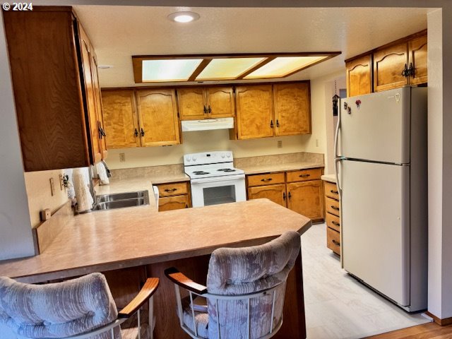 kitchen with kitchen peninsula, light wood-type flooring, a breakfast bar, white appliances, and sink