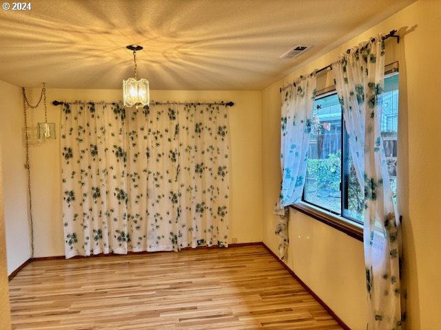 spare room with an inviting chandelier and light wood-type flooring