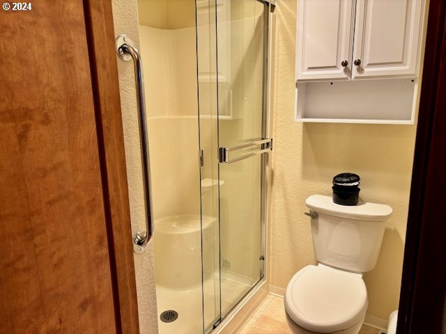 bathroom with tile patterned flooring, toilet, and a shower with door