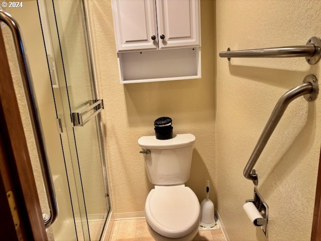 bathroom featuring tile patterned floors, a shower with shower door, and toilet