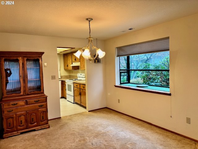 kitchen featuring white range with electric cooktop, light colored carpet, decorative light fixtures, and an inviting chandelier