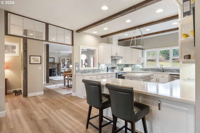 kitchen featuring stainless steel appliances, beamed ceiling, kitchen peninsula, a breakfast bar area, and white cabinets