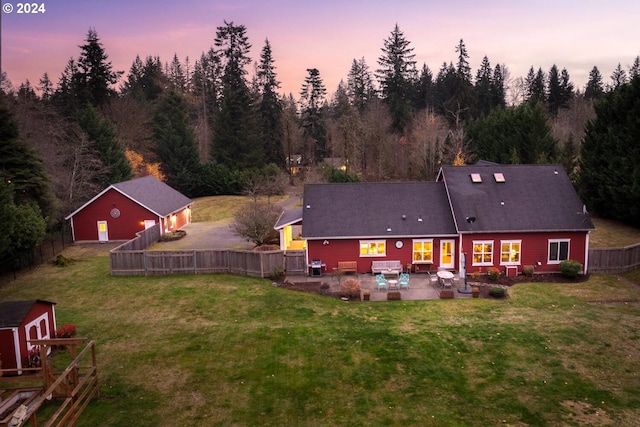 back house at dusk with a yard, a storage unit, and a patio area