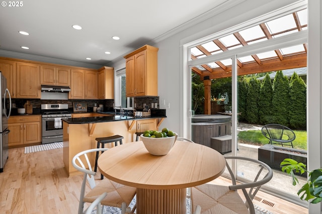 2834 SE Franklin St, Portland, OR 97202 - kitchen featuring appliances with stainless steel finishes, under cabinet range hood, ornamental molding, decorative backsplash, and a peninsula