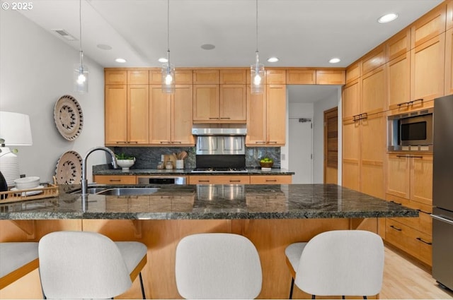 kitchen featuring sink, ventilation hood, hanging light fixtures, dark stone countertops, and appliances with stainless steel finishes