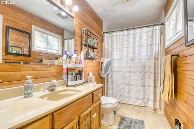 bathroom with vanity, wood walls, tile patterned flooring, toilet, and a textured ceiling