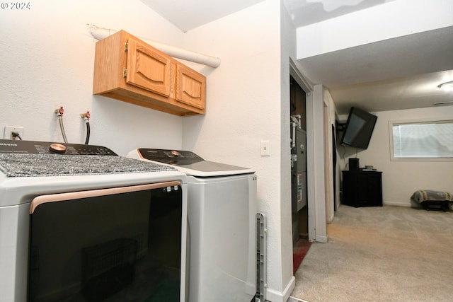 clothes washing area with washing machine and clothes dryer, light colored carpet, and cabinets