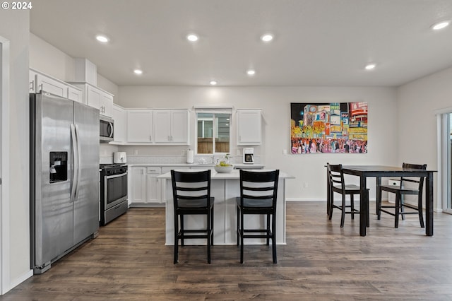 kitchen with stainless steel appliances, dark hardwood / wood-style flooring, white cabinetry, a breakfast bar area, and a kitchen island