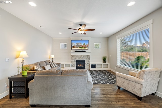 living room with dark hardwood / wood-style floors, a stone fireplace, and ceiling fan