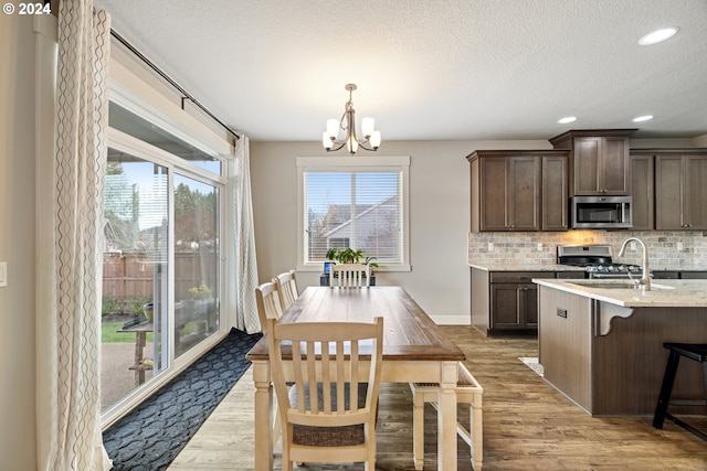 dining space with sink, a chandelier, a textured ceiling, and light hardwood / wood-style flooring