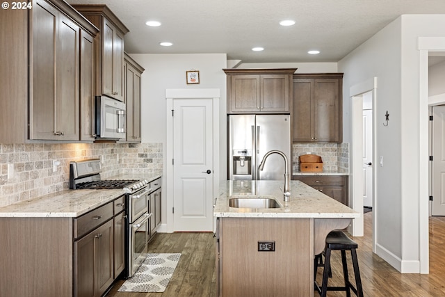 kitchen featuring sink, an island with sink, appliances with stainless steel finishes, dark hardwood / wood-style flooring, and light stone counters