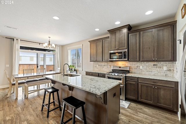 kitchen with a kitchen island with sink, sink, hardwood / wood-style flooring, light stone counters, and stainless steel appliances