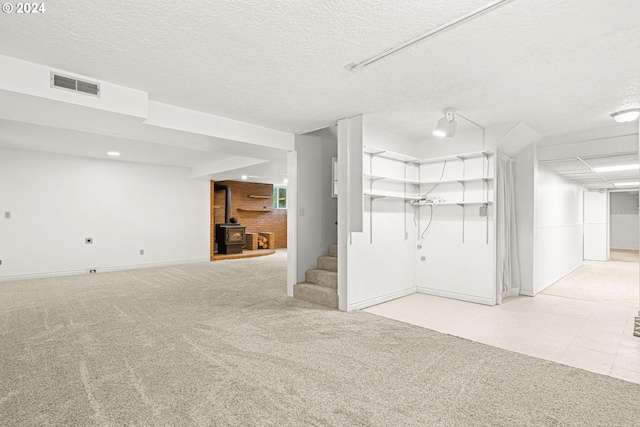 basement with a wood stove, light colored carpet, and a textured ceiling