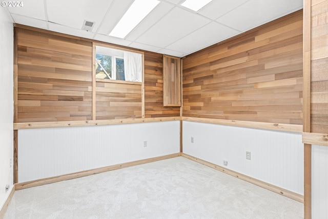 unfurnished room with light carpet, wooden walls, and a paneled ceiling