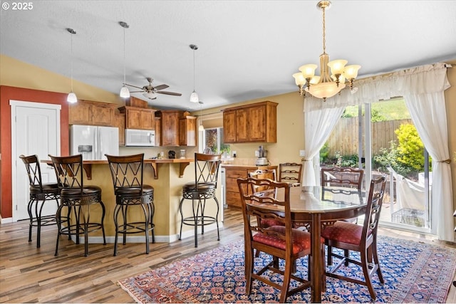 dining room featuring light wood finished floors, baseboards, and ceiling fan with notable chandelier