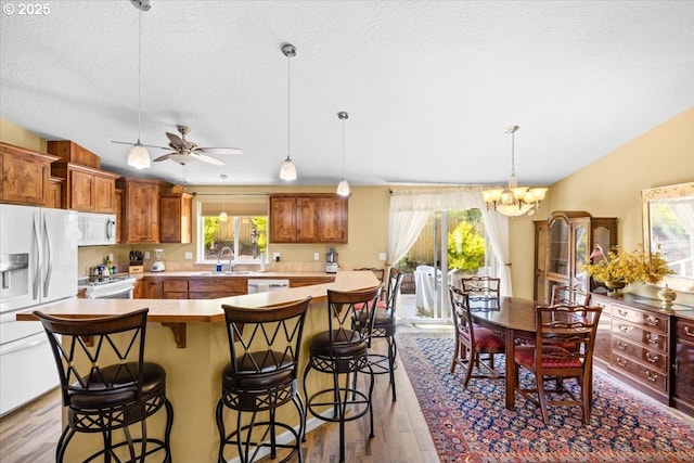 kitchen featuring a sink, white appliances, wood finished floors, a kitchen breakfast bar, and light countertops