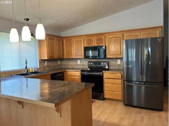 kitchen with hanging light fixtures, sink, black appliances, vaulted ceiling, and light wood-type flooring