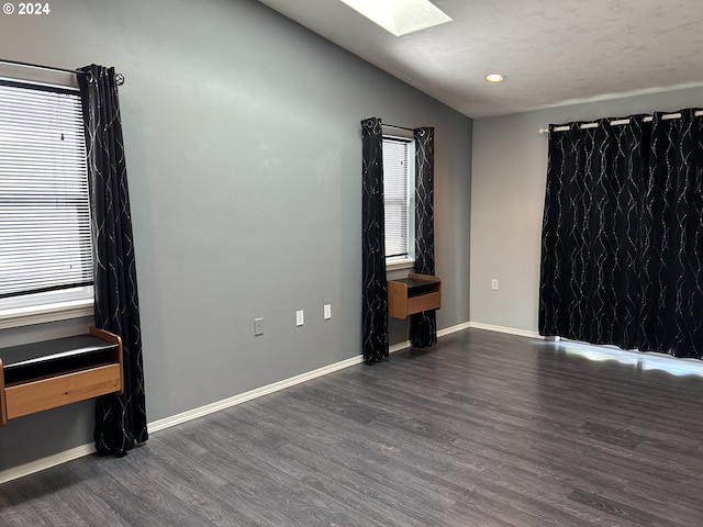 empty room featuring lofted ceiling with skylight and dark hardwood / wood-style floors