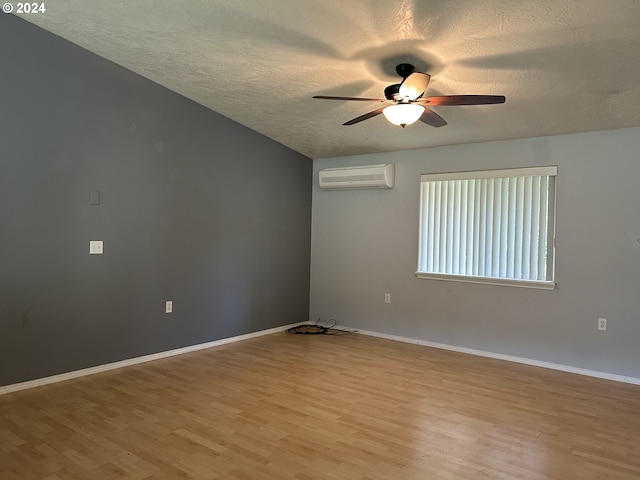 empty room featuring an AC wall unit, light hardwood / wood-style flooring, a textured ceiling, and ceiling fan