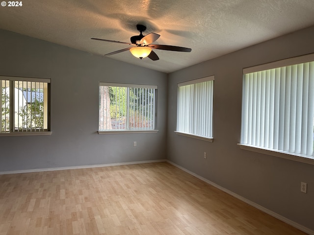 spare room with a wealth of natural light, vaulted ceiling, light hardwood / wood-style flooring, and a textured ceiling