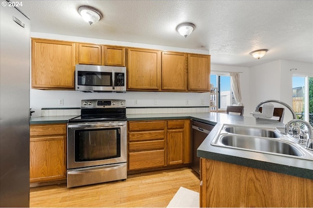 kitchen with sink, a textured ceiling, appliances with stainless steel finishes, and light wood-type flooring