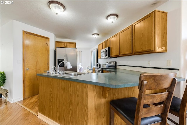 kitchen with kitchen peninsula, light hardwood / wood-style flooring, sink, a textured ceiling, and stainless steel appliances