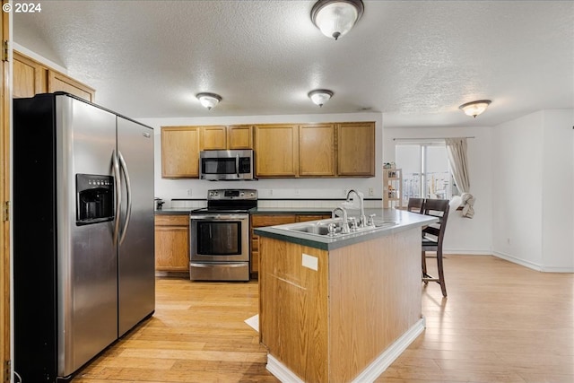 kitchen with light hardwood / wood-style floors, sink, appliances with stainless steel finishes, and a kitchen island with sink