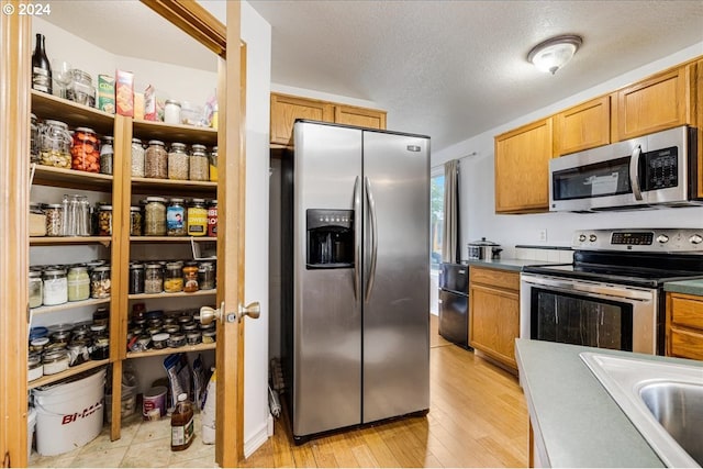 kitchen with sink, a textured ceiling, appliances with stainless steel finishes, and light hardwood / wood-style flooring