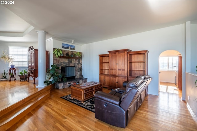 living room with arched walkways, a healthy amount of sunlight, light wood finished floors, and a stone fireplace