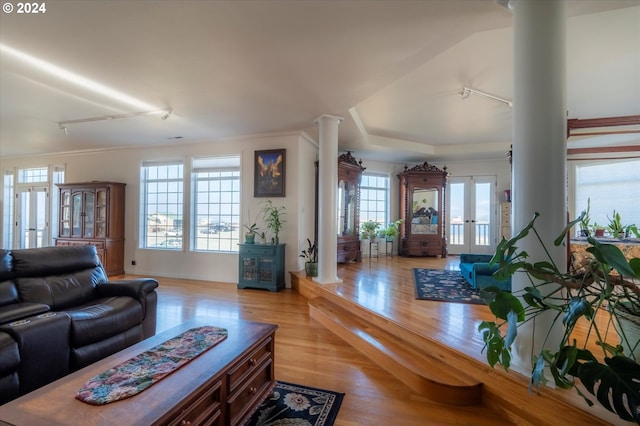 living room with a wealth of natural light, french doors, decorative columns, and light wood-type flooring