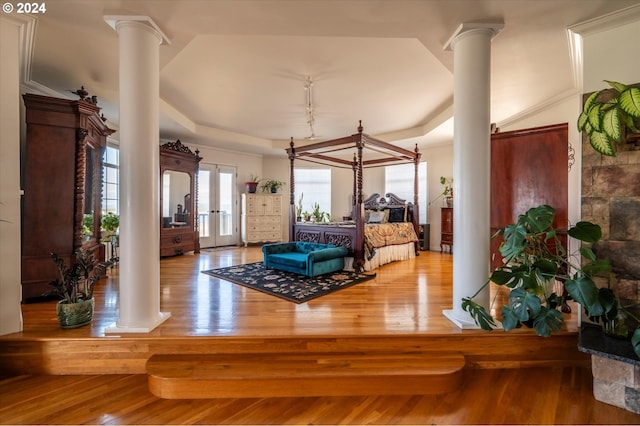 bedroom featuring track lighting, access to exterior, a raised ceiling, decorative columns, and wood finished floors