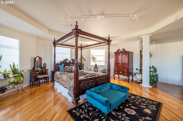 bedroom with ornate columns, hardwood / wood-style flooring, a tray ceiling, and rail lighting