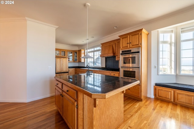 kitchen featuring light wood-type flooring, a center island, stainless steel double oven, pendant lighting, and a breakfast bar area