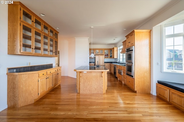 kitchen with ornamental molding, glass insert cabinets, a kitchen island, stainless steel double oven, and light wood-style floors