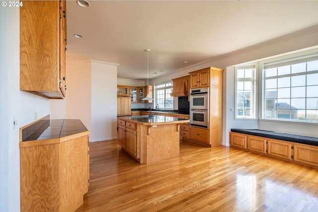 kitchen featuring ornamental molding, a kitchen island, stainless steel double oven, and light hardwood / wood-style flooring