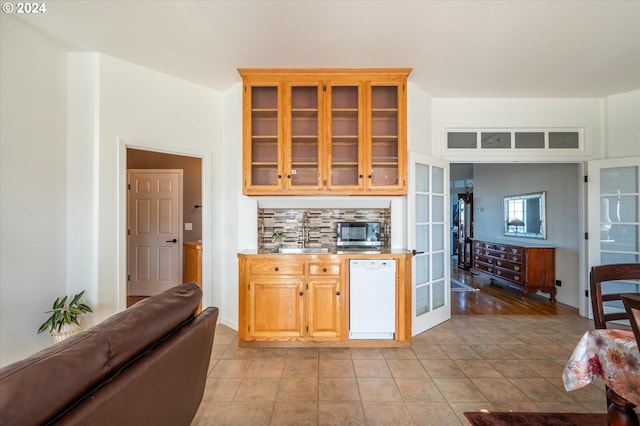 kitchen featuring stainless steel microwave, tasteful backsplash, glass insert cabinets, dishwasher, and a sink