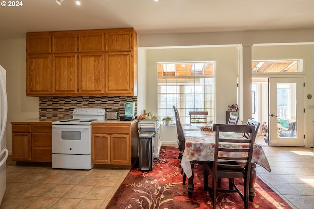kitchen with light tile patterned floors, light countertops, electric stove, brown cabinets, and backsplash