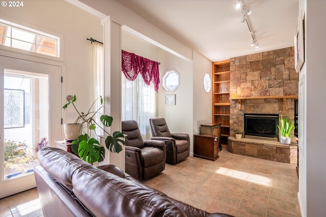 tiled living area with track lighting, built in features, a stone fireplace, and plenty of natural light