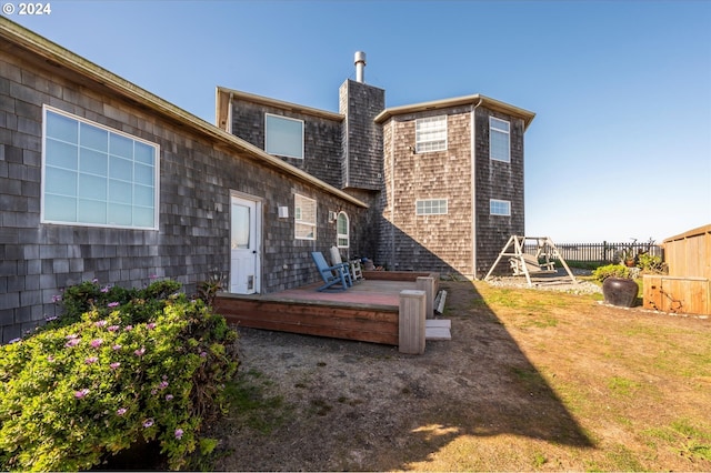 back of property featuring a chimney, a wooden deck, fence, and a yard